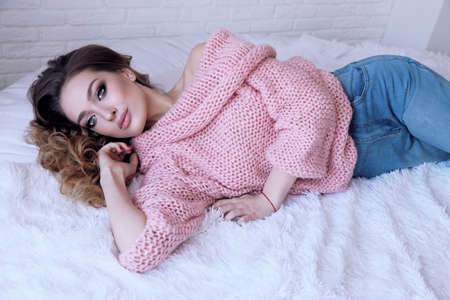 fashion photo of beautiful young girl with blond curly hair in cozy clothes posing in studioの写真素材