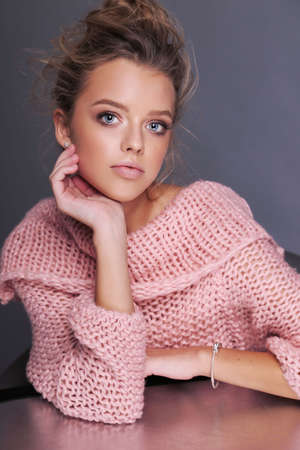 fashion photo of beautiful young girl with blond hair in cozy pink cardigan posing in studioの写真素材