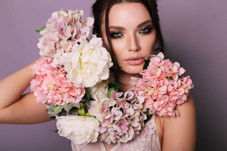 fashion photo of beautiful girl with dark hair in elegant outfit posing among spring flowers in studioの写真素材