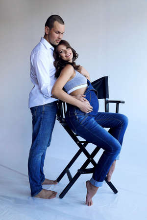 fashion photo of handsome man and beautiful pregnant woman in casual clothes posing at studioの写真素材