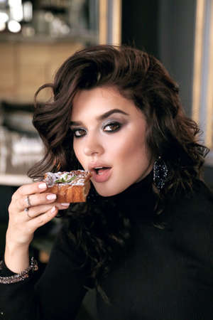 fashion photo of beautiful young woman with dark curly hair in elegant dress sitting in elegant restaurantの写真素材
