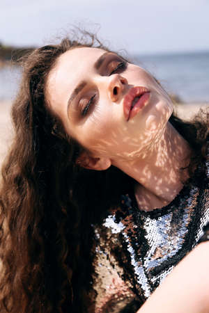 fashion outdoor photo of beautiful girl with dark curly hair in elegant shiny dress with sequins...