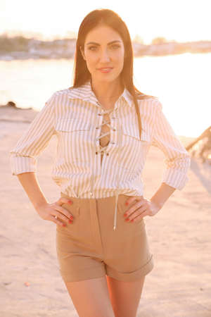 Fashion outdoor photo of beautiful woman with dark hair in elegant clothes posing on sunset beachの写真素材