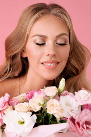 fashion interior photo of beautiful young woman with blond curly hair in elegant clothes posing with bouquet of spring flowersの写真素材