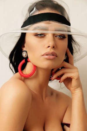 fashion studio portrait of beautiful woman with dark hair in fashion transparent hat and luxurious earringsの写真素材