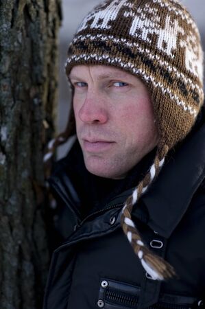 Man in winter hat leaning on treeの写真素材