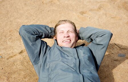 Smiling man laying on the sandの写真素材