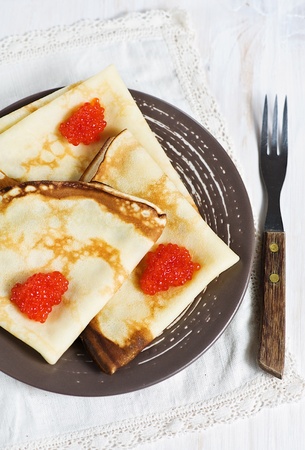 Pancakes with red caviar on the brown plate and forkの写真素材