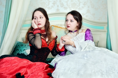Two women sisters in medieval dresses on the bedの写真素材