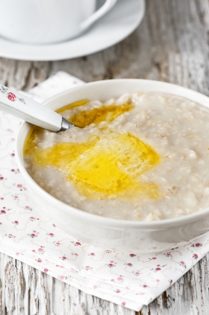 A bowl of hot oatmeal with butter on the old wooden backgroundの写真素材