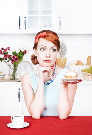 Sad beautiful young woman looking on cake in the kitchenの写真素材