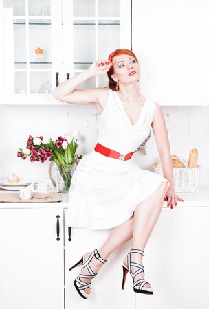 Beautiful woman with red hair sitting on the kitchen table の写真素材
