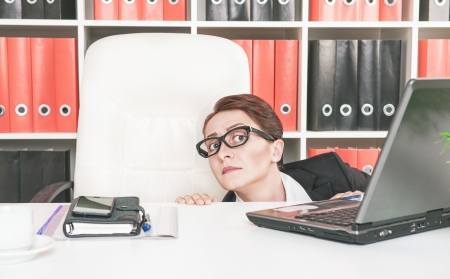 Business woman hiding behind table and afraidの写真素材