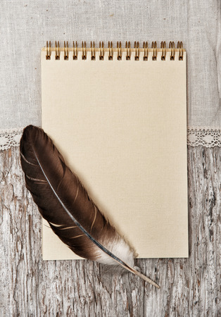 Paper spiral notebook, feather  and linen fabric on the old wooden backgroundの写真素材