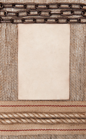 Aged paper with sacking ribbon, metal chain and rope on burlap background の写真素材