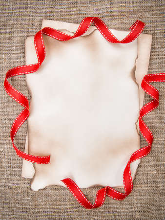 Christmas card with aged paper and red ribbon on burlap backgroundの写真素材