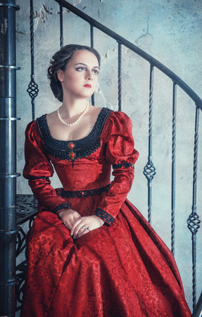 Beautiful young woman in red medieval dress on the stairwayの写真素材