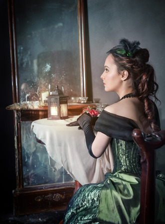 Beautiful young woman in green medieval dress sitting near mirror Beautiful young woman in green medieval dress sitting near mirror