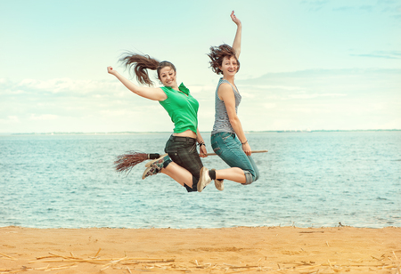 Two happy young women with broom jumping on the beach outdoorの写真素材