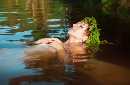 Young beautiful drowned woman with fern wreath lying in the waterの写真素材