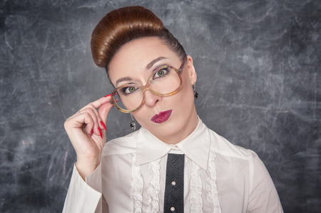 Strict teacher in eyeglasses looking on someone at the school blackboard backgroundの写真素材