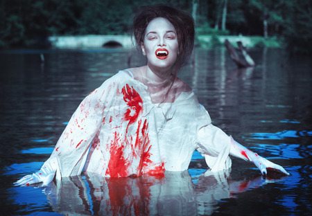 Beautiful vampire woman dressed white bloody shirt standing in the riverの写真素材