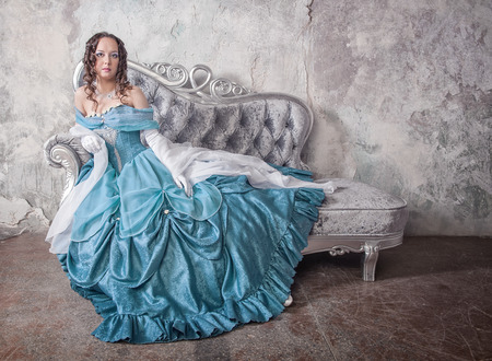 Beautiful young woman in blue medieval dress on the sofaの写真素材