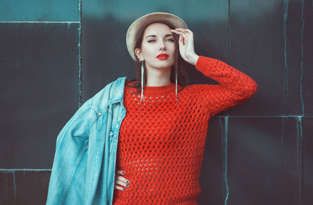 Young beautiful girl in red jersey with hat outdoor near wallの写真素材