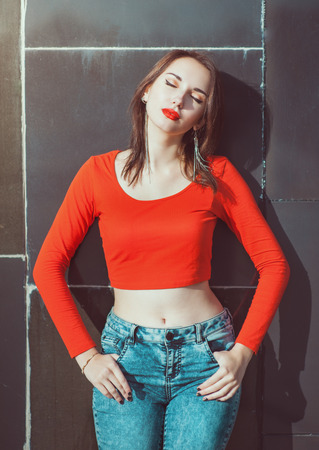 Young beautiful girl in red blouse enjoy sunlight outdoor near wallの写真素材