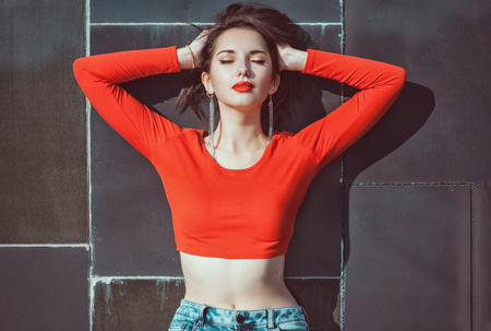 Young beautiful girl in red blouse enjoy sunlight outdoor near wallの写真素材