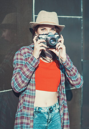 Hipster girl in hat making picture with retro camera outdoor. Focus on cameraの写真素材