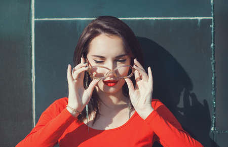 Young beautiful girl in red blouse and glasses outdoor near wallの写真素材