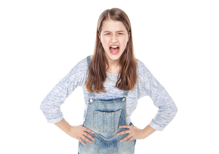 Angry young fashion girl in jeans overalls screaming isolated on white backgroundの写真素材