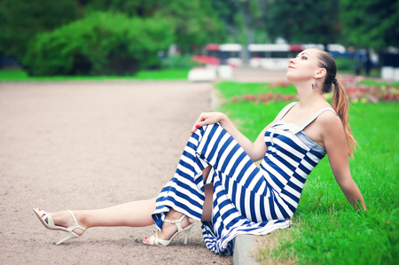 Young beautiful fashionable woman wearing striped dress sitting on the lawnの写真素材