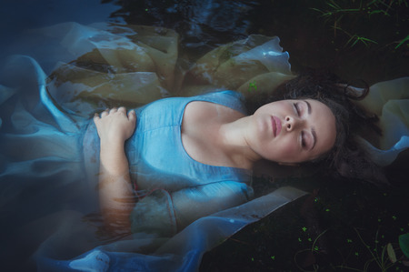 Young beautiful drowned woman in blue dress lying in the water outdoorの写真素材
