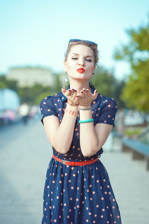 Beautiful young hipster woman in fifties style sending kiss in the cityの写真素材