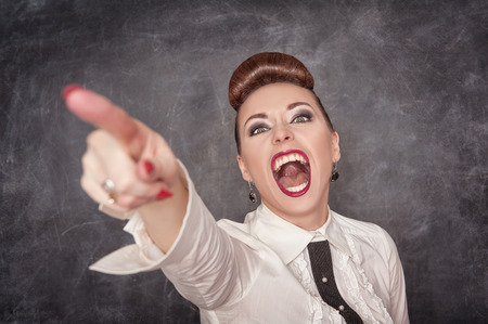 Angry screaming woman in white blouse pointing out on the chalkboard background