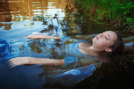 Young beautiful drowned woman in blue dress lying in the water