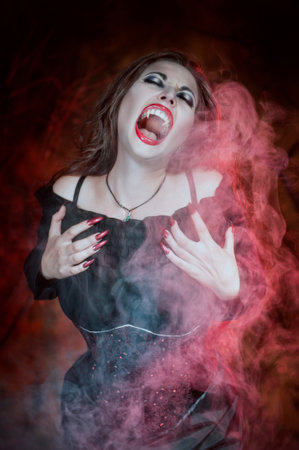 Screaming halloween beautiful vampire with long hair in smokeの写真素材