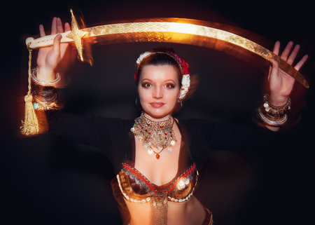 Beautiful exotic belly tribal dancer woman with sword on black background