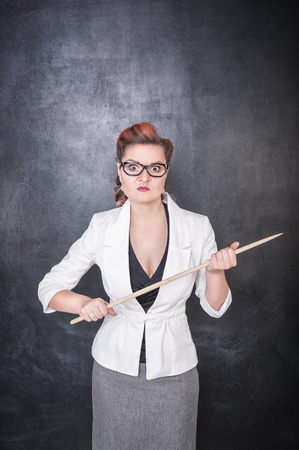 Serious teacher in glasses with pointer on the chalkboard blackboard backgroundの写真素材
