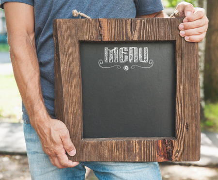 Restaurant menu on wooden board hold by man hand outdoor. Template mock upの写真素材
