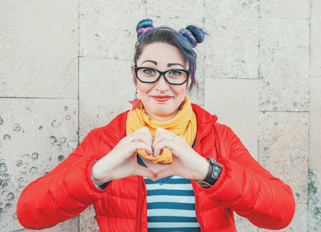 Happy beautiful fashion hipster woman with colorful hair showing heart by handsの写真素材
