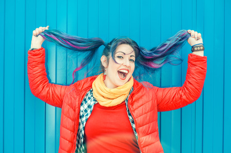 Young beautiful fashion hipster woman with colorful hair having fun over blue backgroundの写真素材