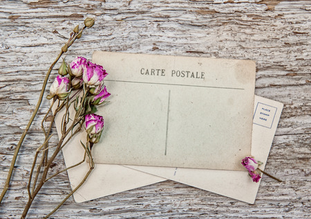 Vintage postcard and dry tea roses on the old wooden background