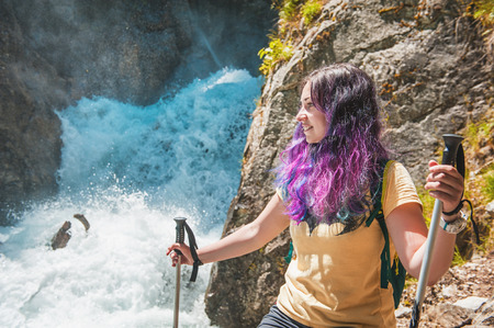 Woman hiker with sticks looking on waterfall outdoor. Tourism conceptの写真素材