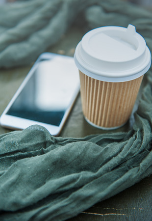 Paper cup of coffee, green scarf and mobile phone on wooden backgroundの写真素材