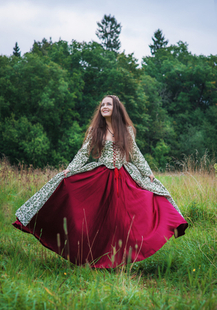 Beautiful happy woman in long medieval dress dancing outdoorの写真素材