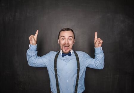 Amazed  businessman or teacher having idea and fingers up on blackboard background