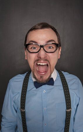 Angry screaming teacher man in eyeglasses on blackboard backgroundの写真素材